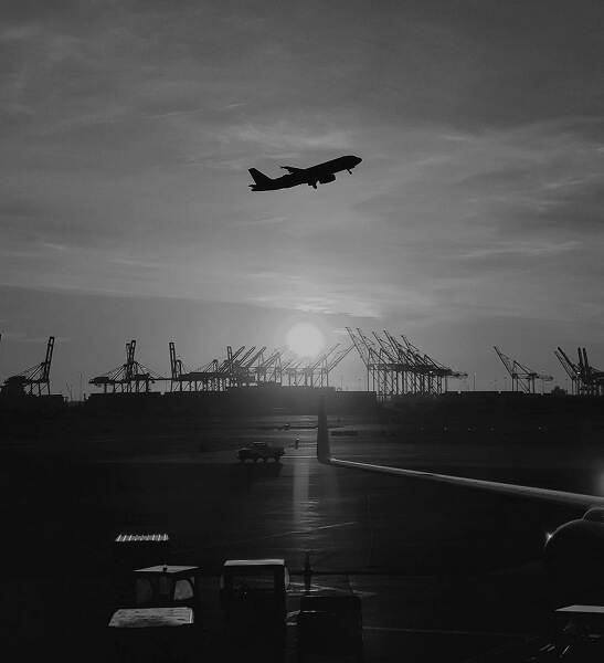 Silhouette of an airplane taking off against a setting sun with cranes and airport ground equipment in the background.