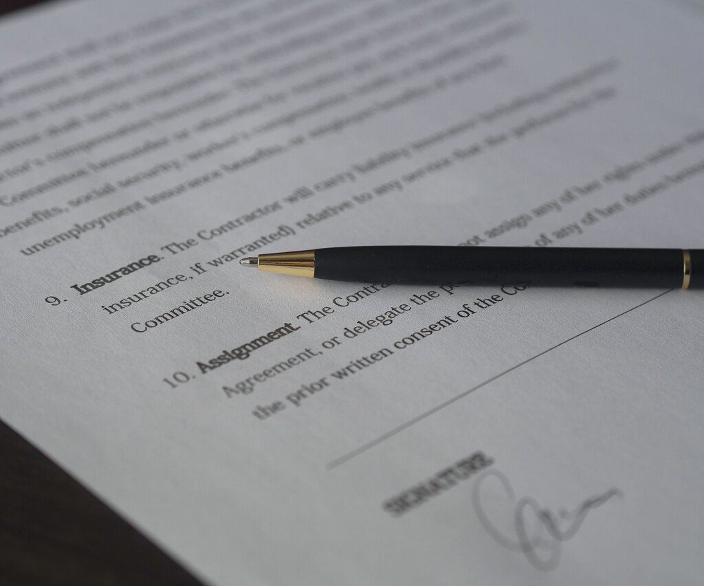 Black pen resting on a contract document with visible sections on insurance and assignment, including a signature line.